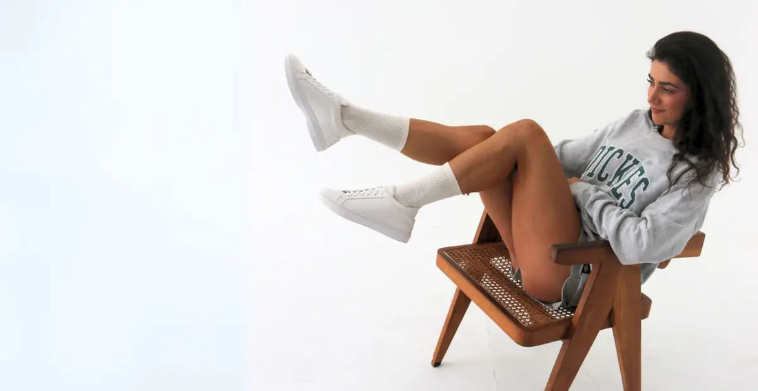 Person seated in a wooden chair wearing white low-top sneakers.