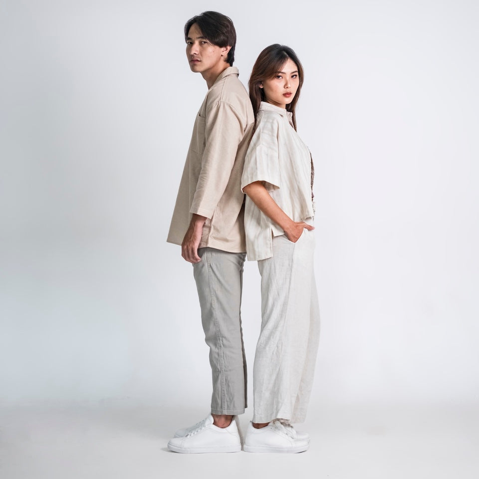 Two people wearing matching beige outfits standing back-to-back on a white background