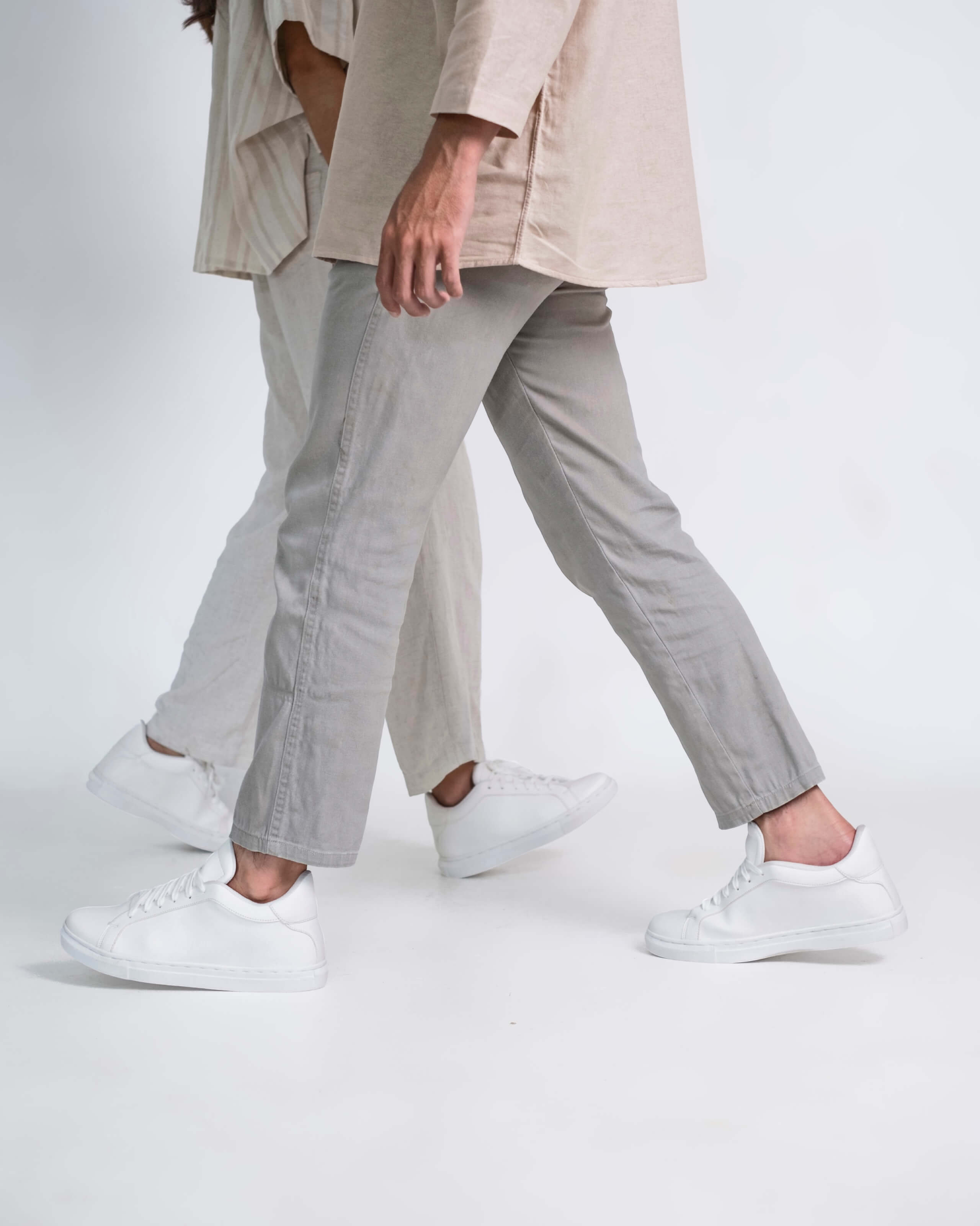 Person wearing a beige outfit with white sneakers on a plain background