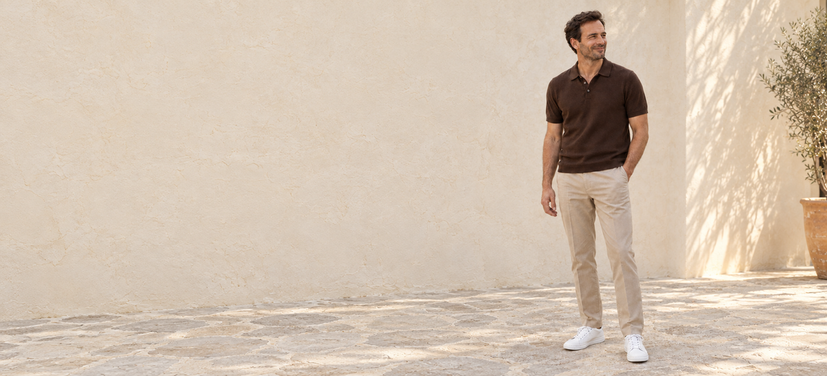 Man wearing white Kosen elevator sneakers with a brown knit polo and beige trousers in a sunlit courtyard.