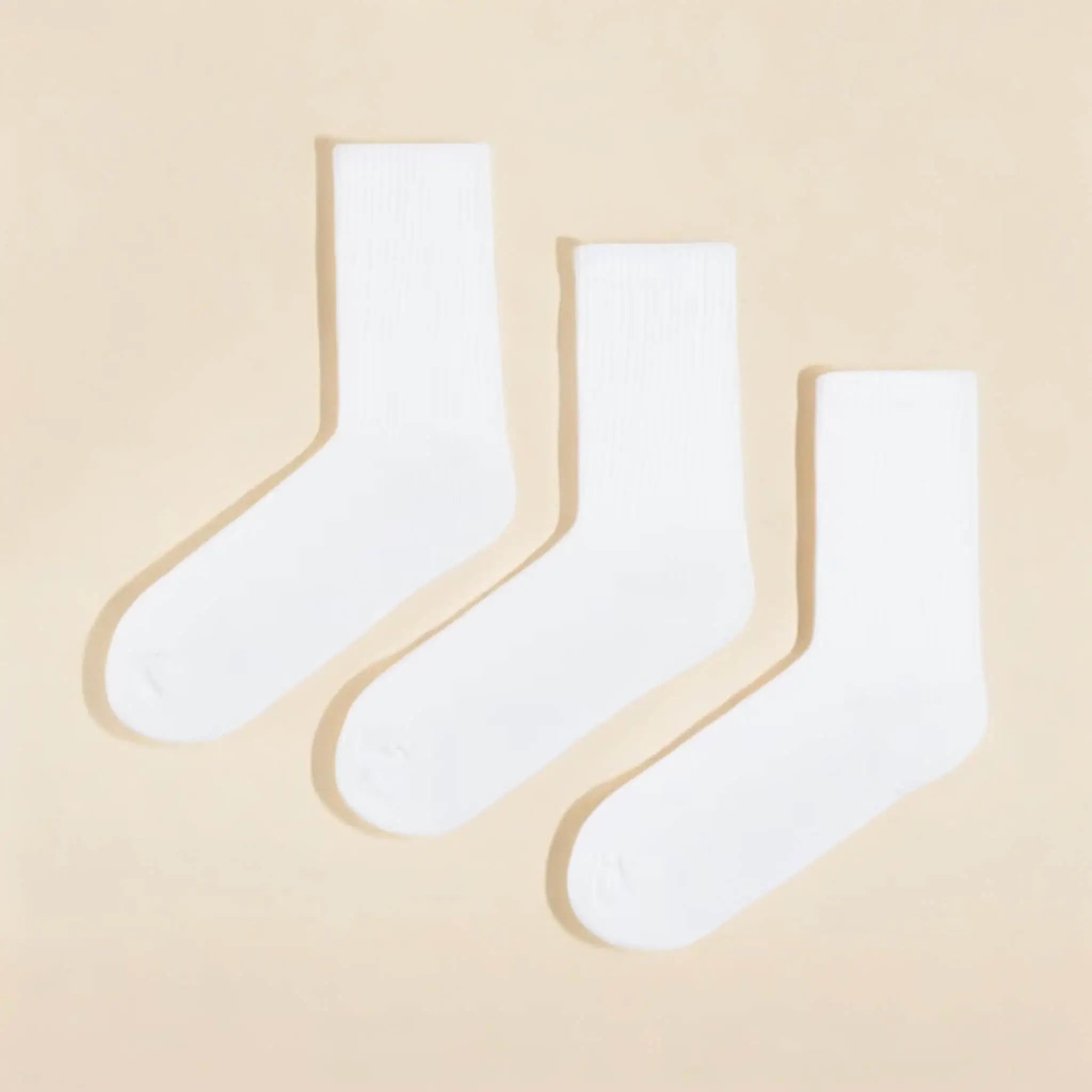 Three pairs of plain white cotton calf socks neatly arranged on a soft beige background for everyday wear