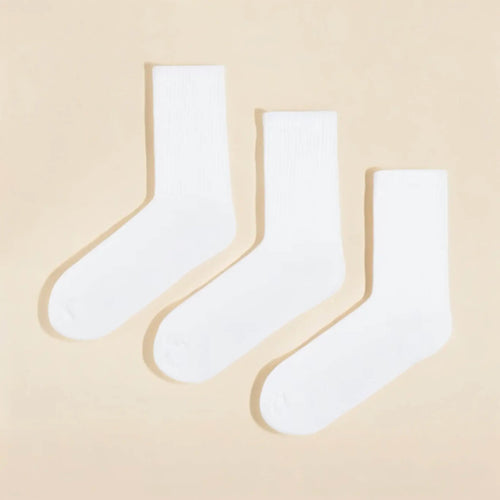 Three pairs of plain white cotton calf socks neatly arranged on a soft beige background for everyday wear